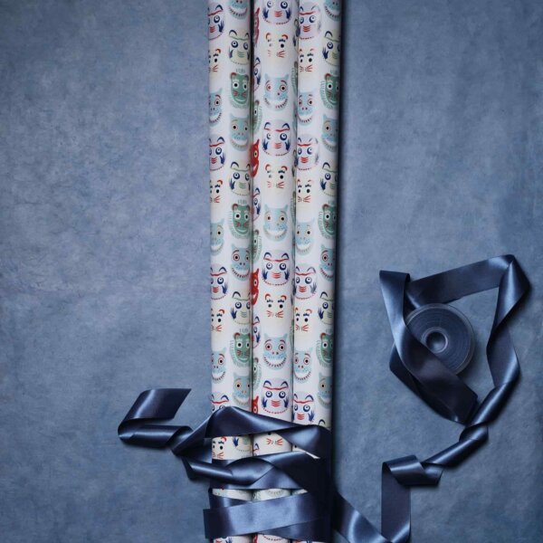 Dancing Masks gift wraps x3 tied up with a large satin dark blue ribbon on blue grey background by Impression Originale