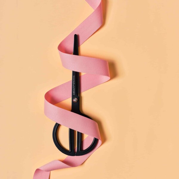 Scissors with a ribbon swirl around it on peachy background by Impression Originale