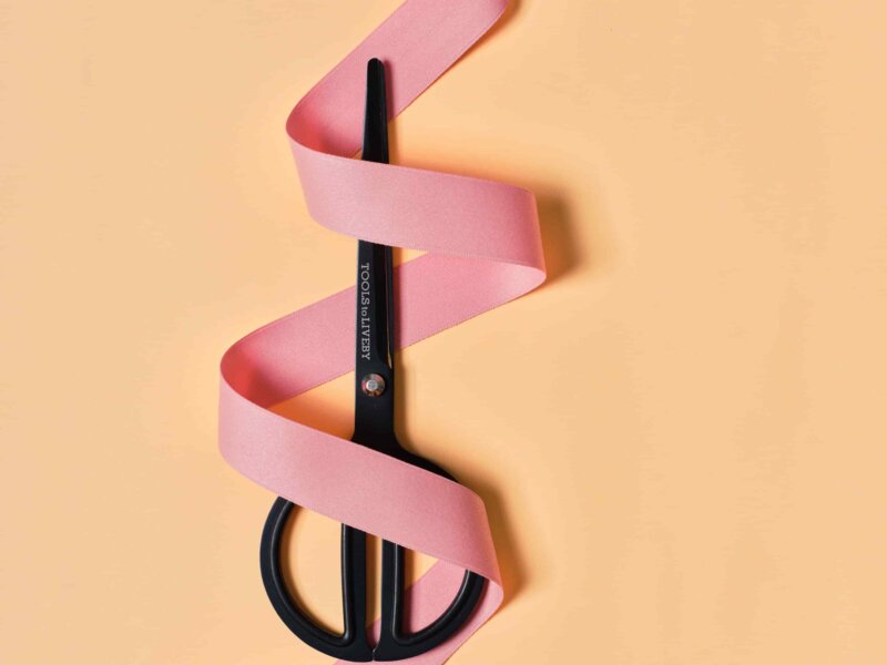 Scissors with a ribbon swirl around it on peachy background by Impression Originale