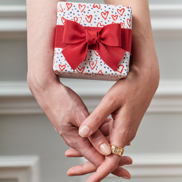 two interweaved hands holding an impression originale gift with a red bow